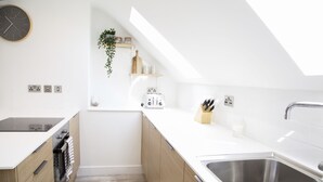 A modern kitchen with a skylight, wooden cabinets, a built-in oven, and a stainless steel sink. - Barber Shop Flat (Stockport)