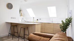 A modern kitchen with a central island, bar stools, and a sofa. - Barber Shop Flat (Stockport)