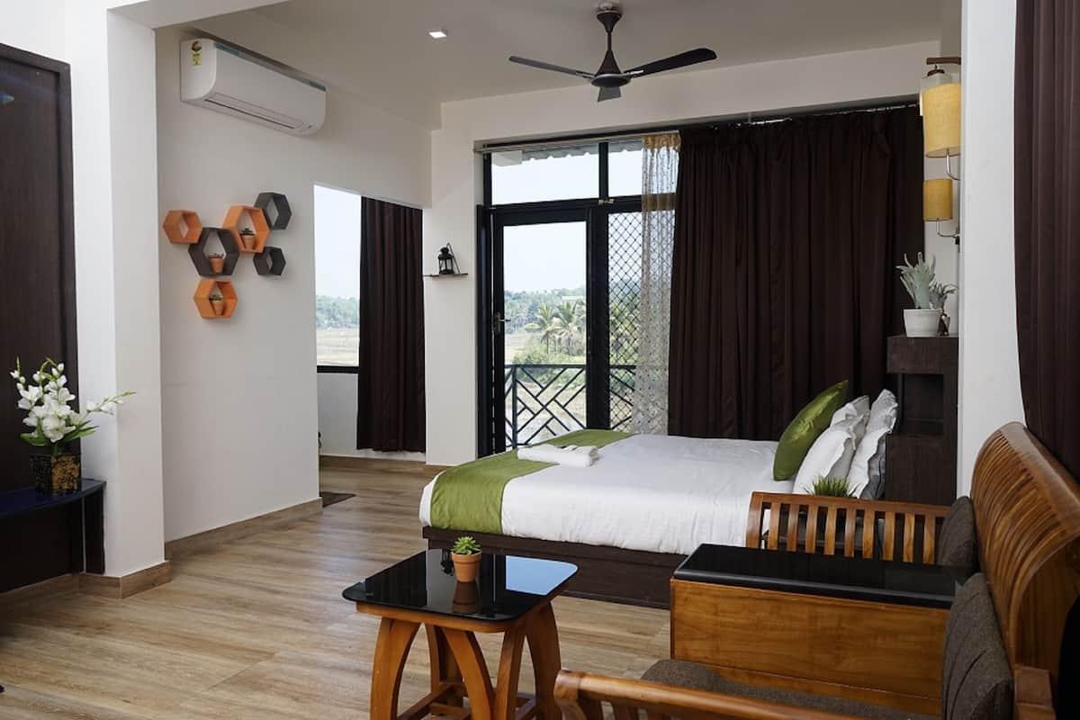 A hotel room with a bed, a wooden bench, a small table, and a balcony with a view.