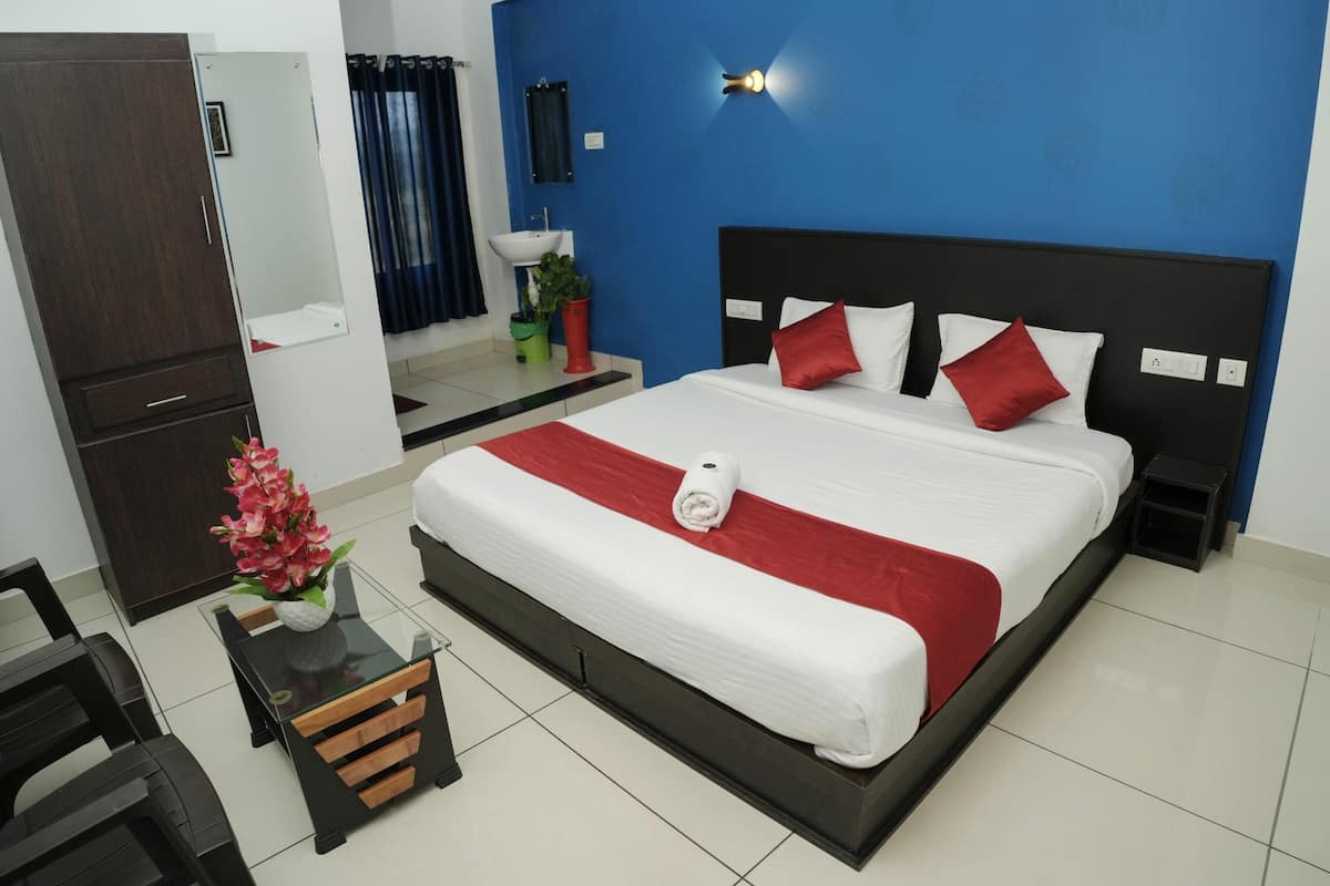 A hotel room with a bed, a desk, a chair, a wardrobe, a mirror, a sink, and a potted plant.