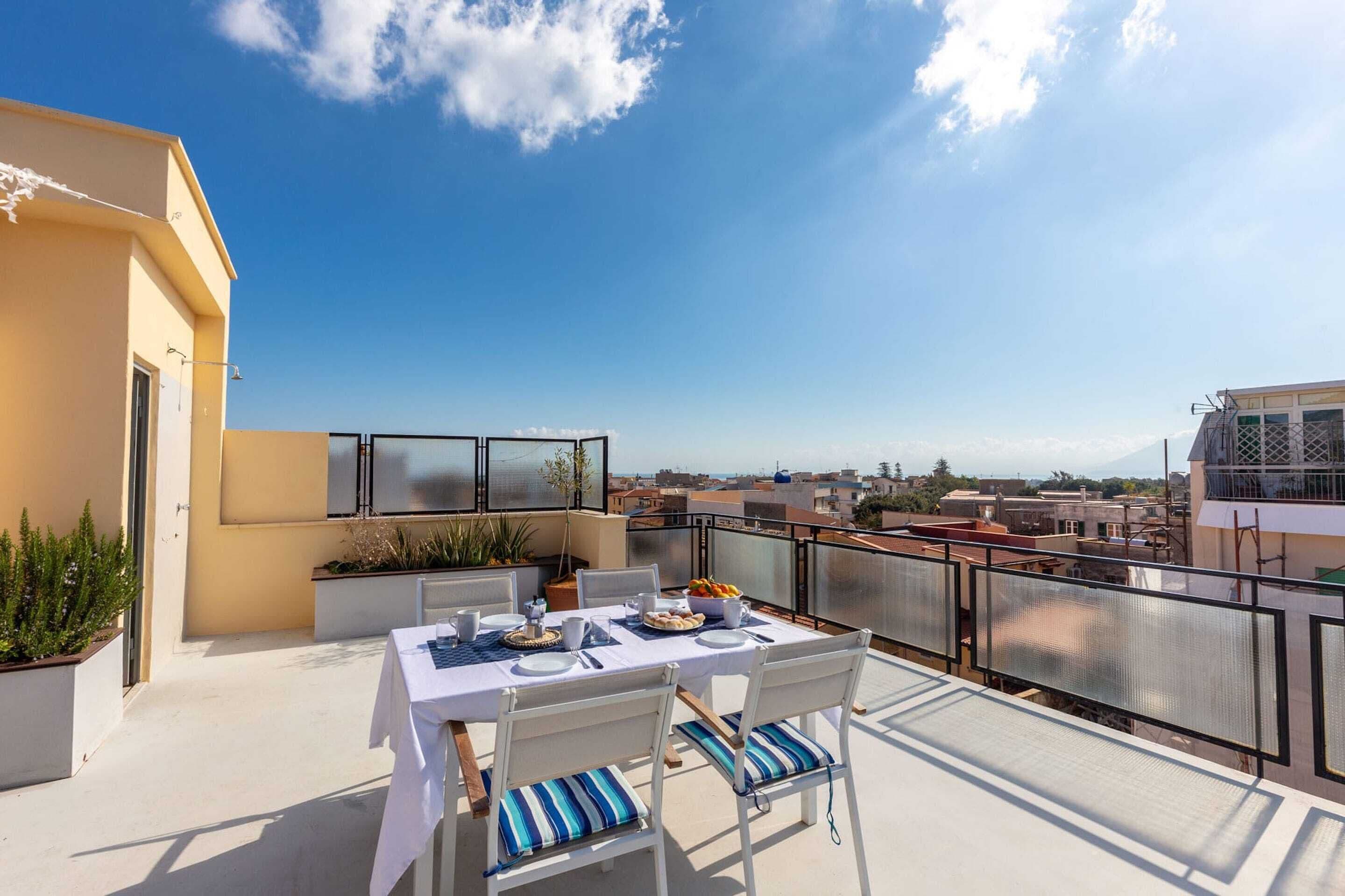A rooftop terrace with a table set for two, outdoor seating, and a view of the cityscape.