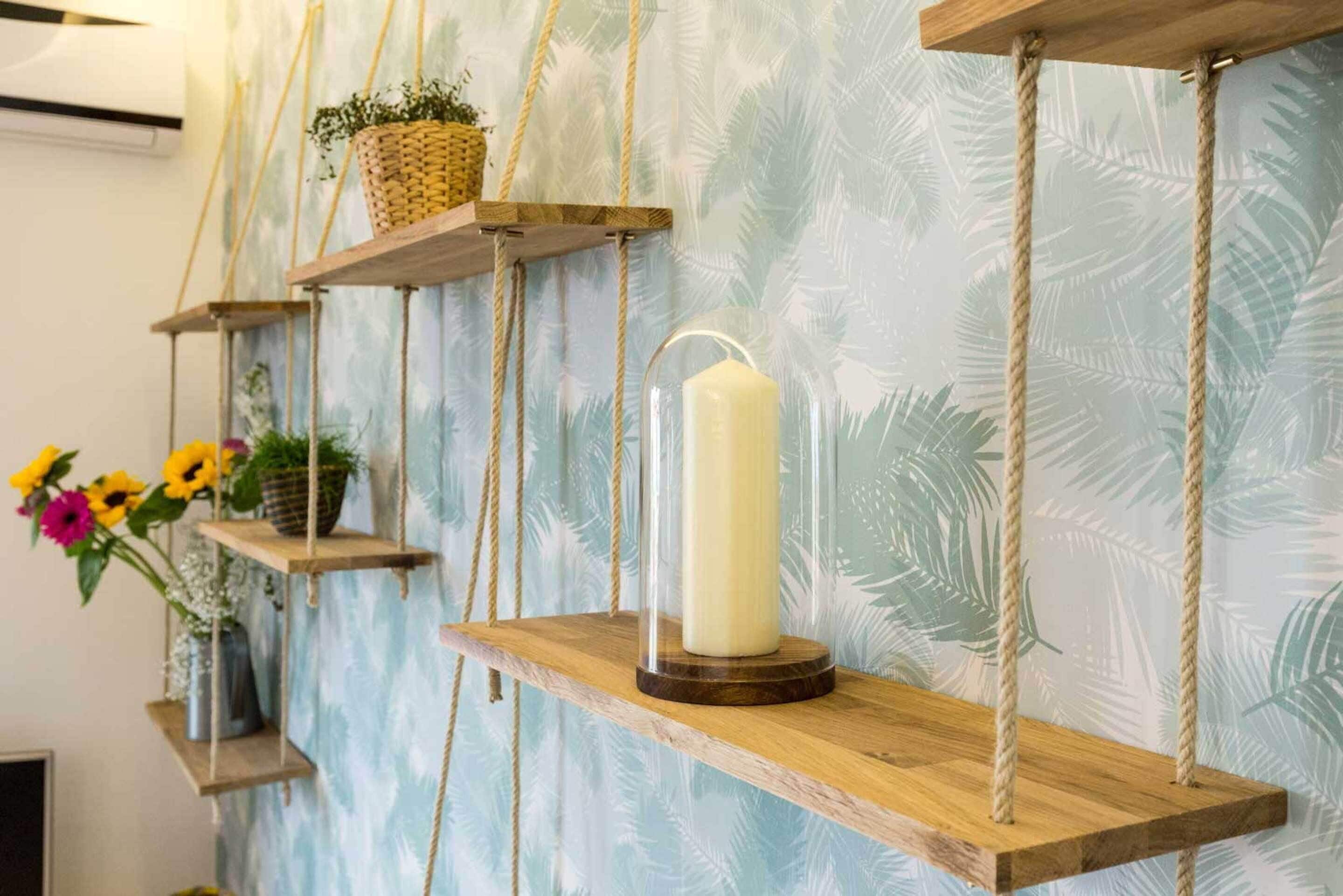 Una stanza con uno scaffale di legno che contiene una candela, un cesto appeso e un vaso con fiori.