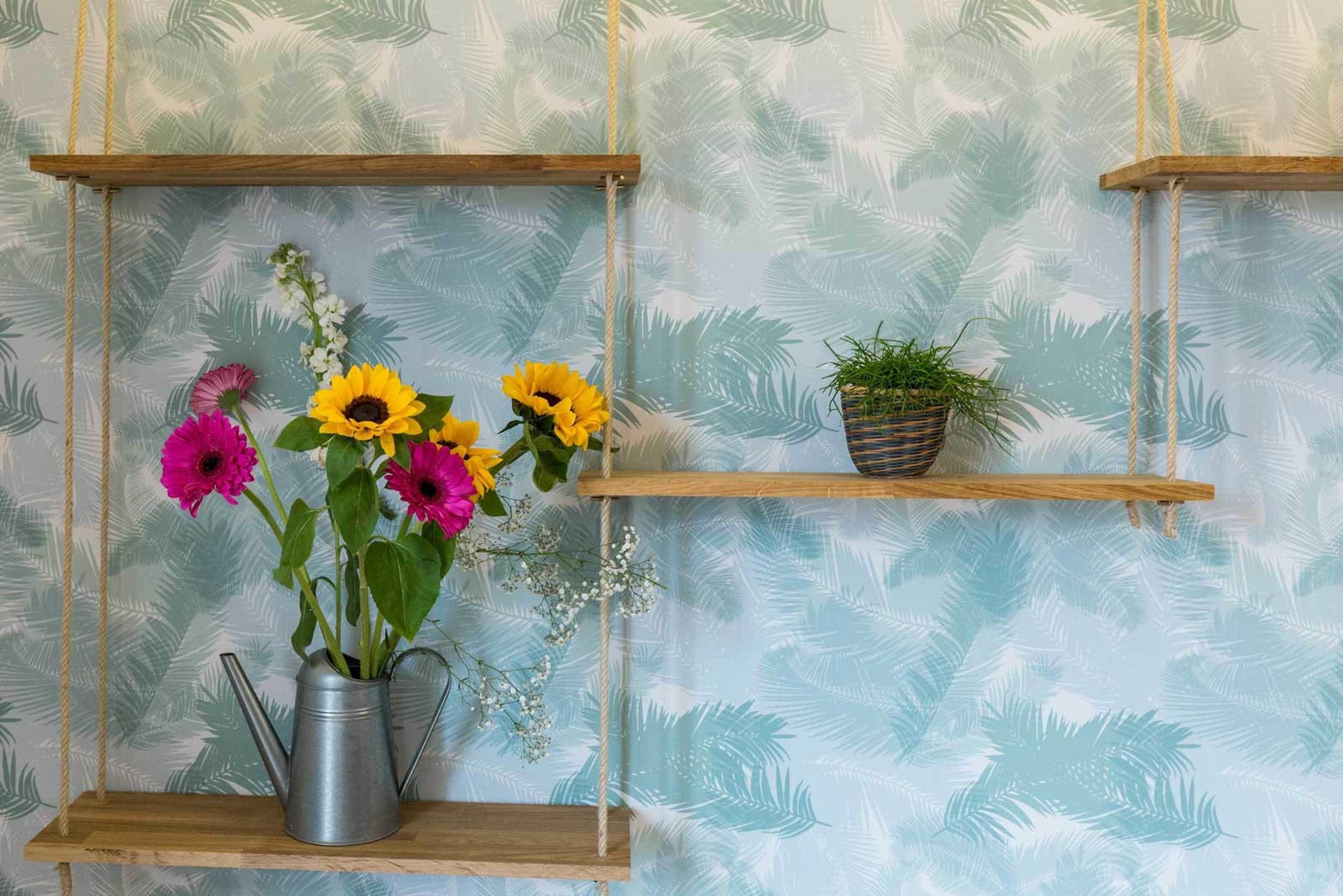 Una pared con papel tapiz estampado con hojas tropicales y tres estantes de madera.