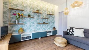 A modern living room with a patterned wallpaper, wooden shelves, a grey sofa, and a woven ottoman. - Solemar Sicilia - Casa Colibrì (Santa Flavia)