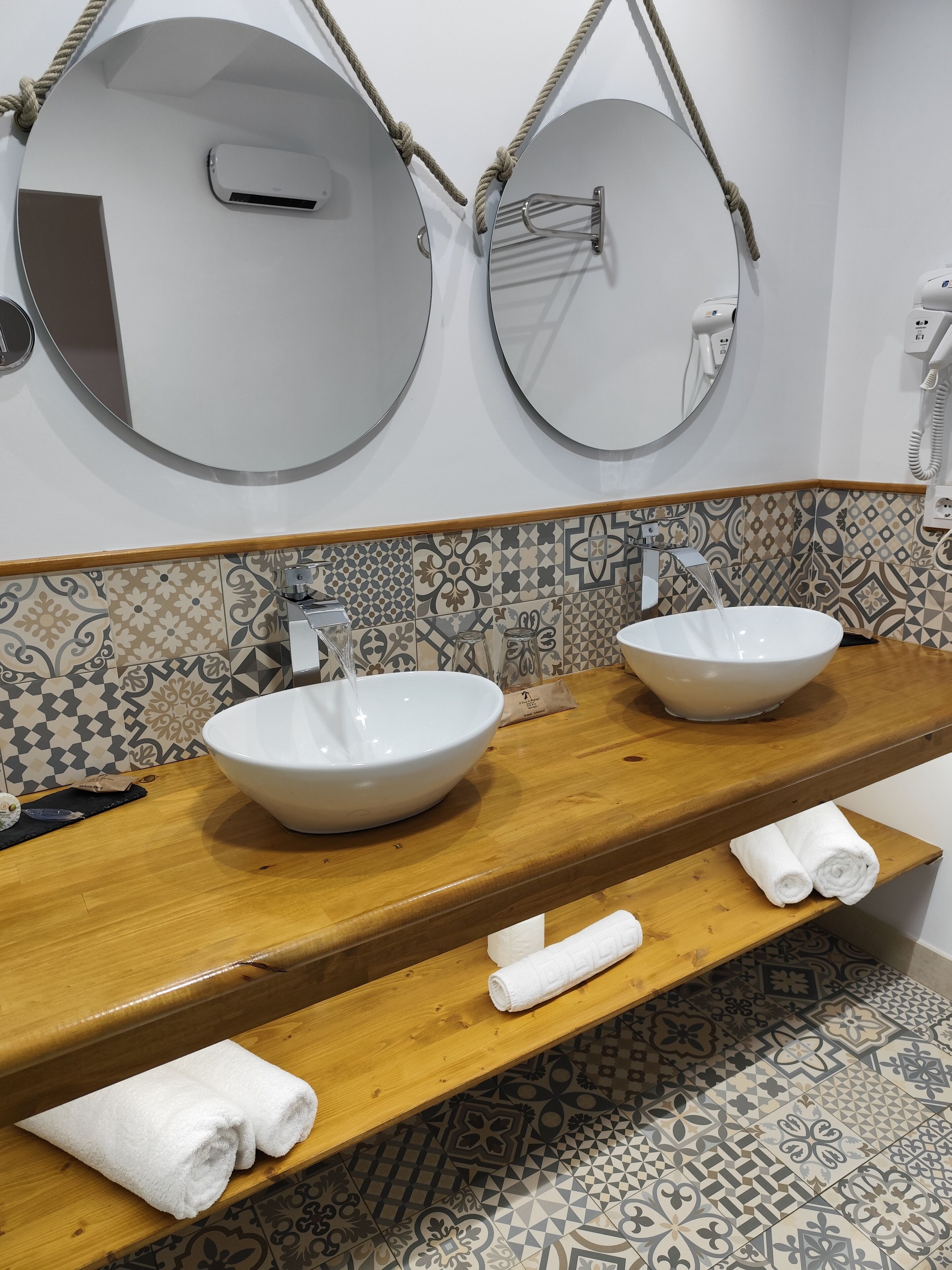 A bathroom with two sinks, a wooden vanity, and a patterned tile backsplash.