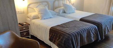 A hotel room with two beds, a wooden floor, a chair, a nightstand, and a small table.