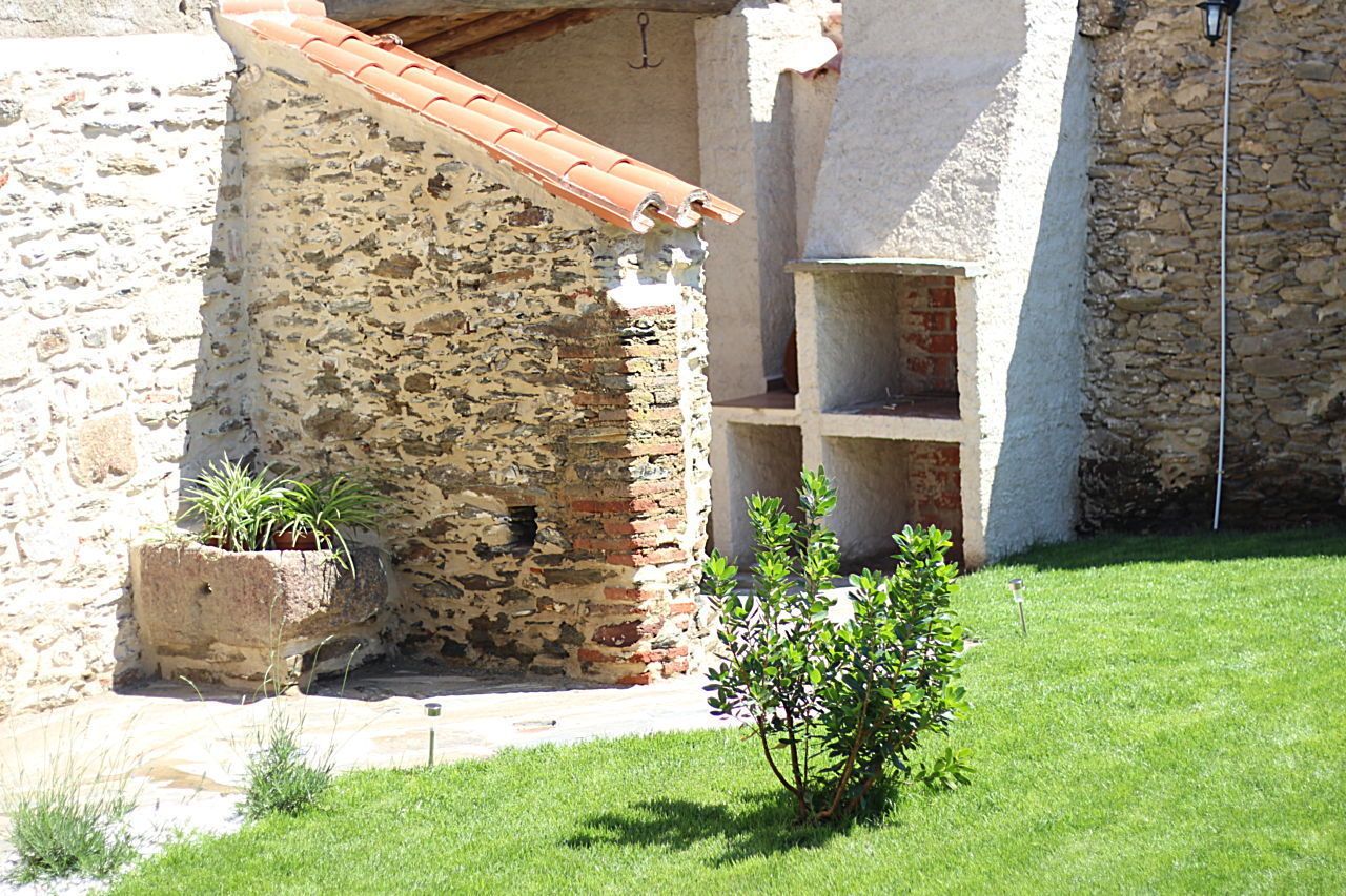 Un edificio de piedra con tejado de tejas, una ventana pequeña y una jardinera con plantas.