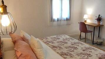 A bedroom with a bed, a desk, and a chair. There is a window with curtains, a lamp, and an air conditioning unit on the wall.