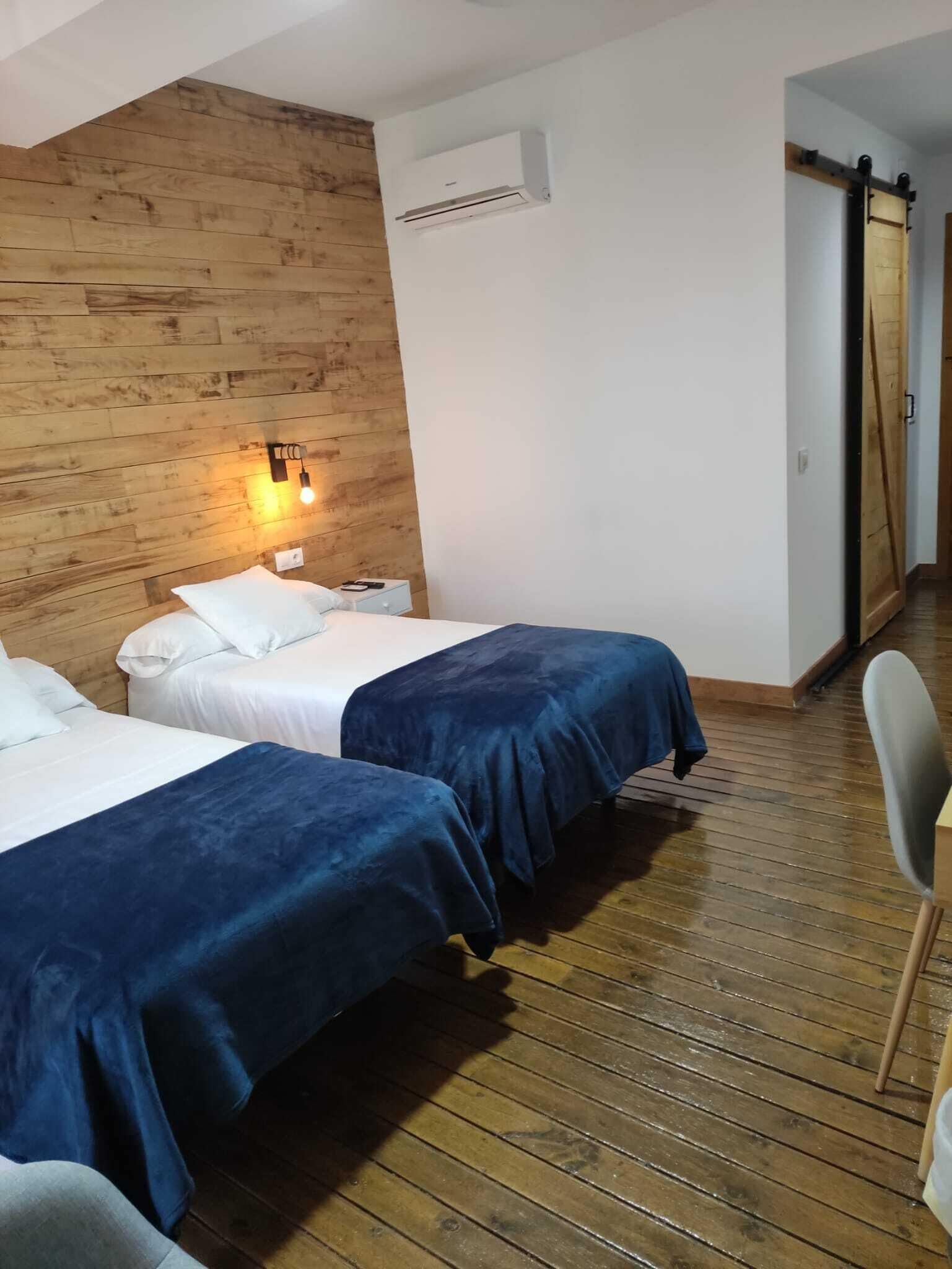 Une chambre avec deux lits, un plancher en bois, un climatiseur fixé au mur et une porte coulissante.