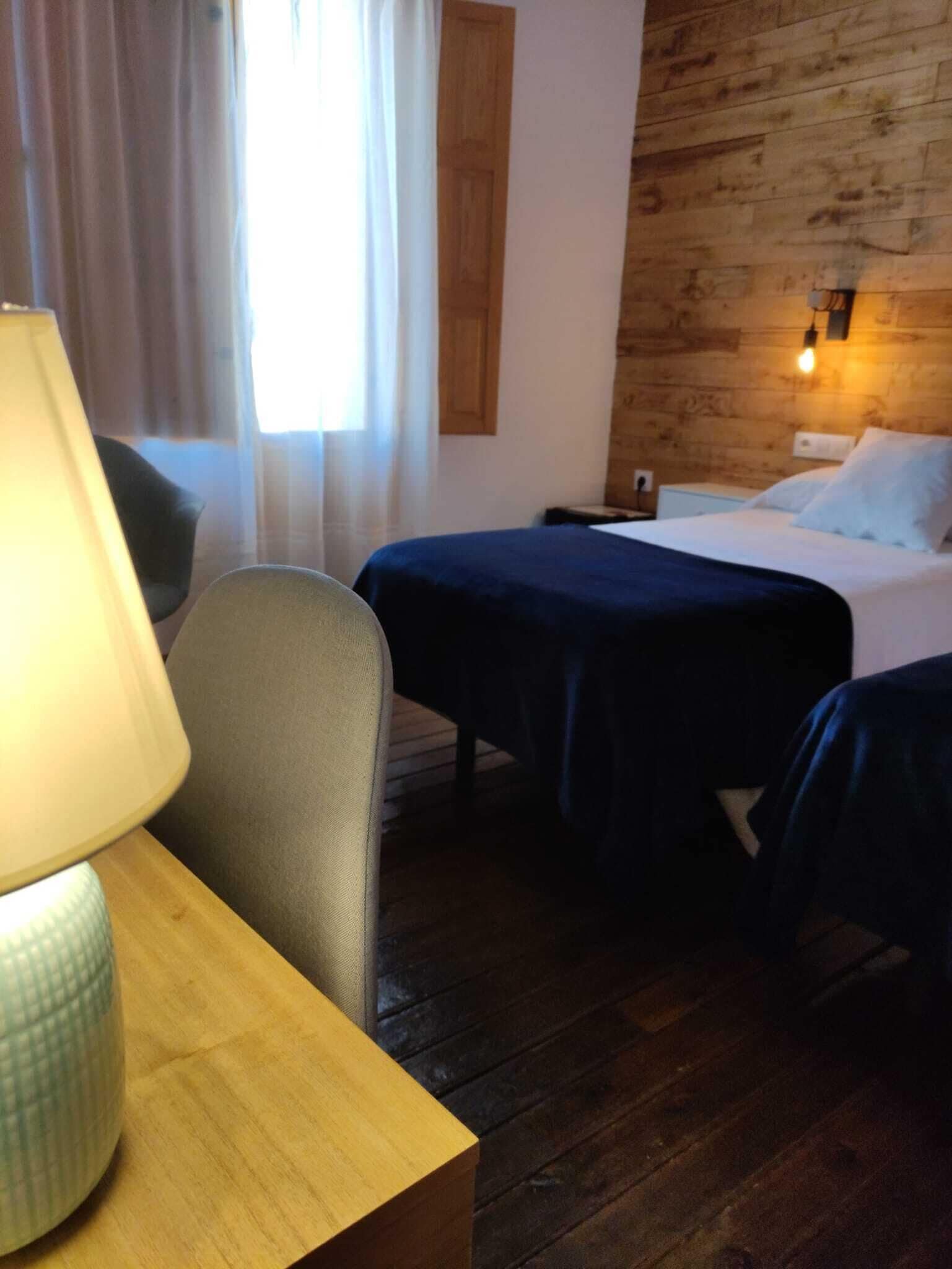 A hotel room with two beds, a wooden headboard, a desk with a lamp, and a window with curtains.