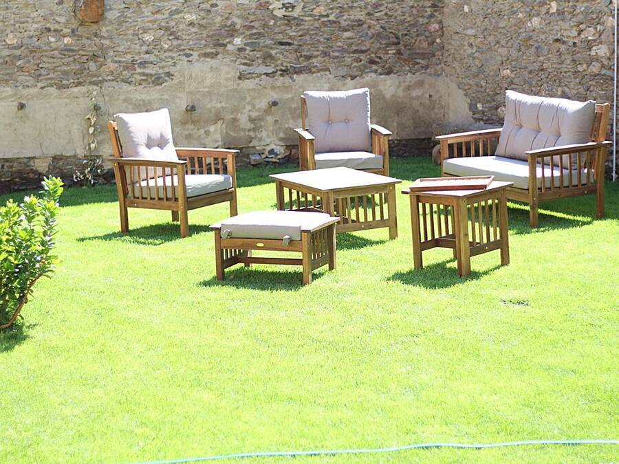 A patio area with wooden furniture including chairs and a table, set against a stone wall.
