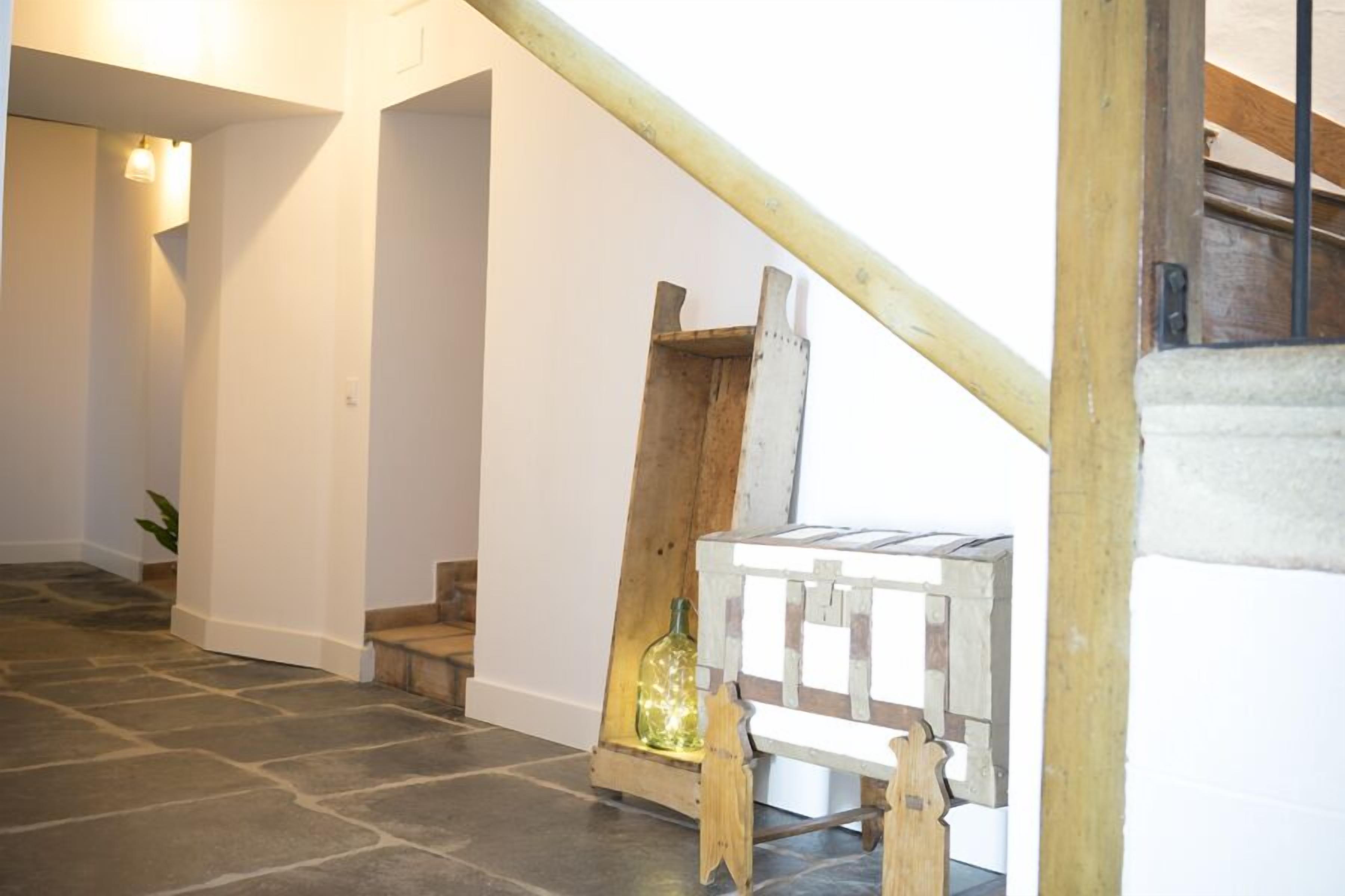 A hallway with a wooden staircase, a small wooden bench, and a bottle on the floor.