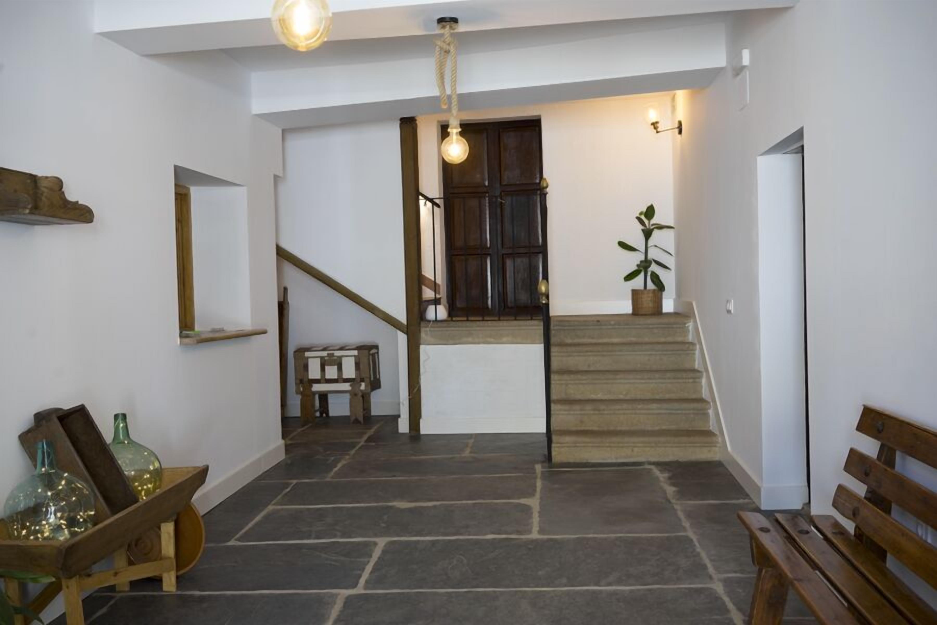 A staircase leading to a dark wooden door, a bench, and a potted plant in a hallway with stone flooring and white walls.