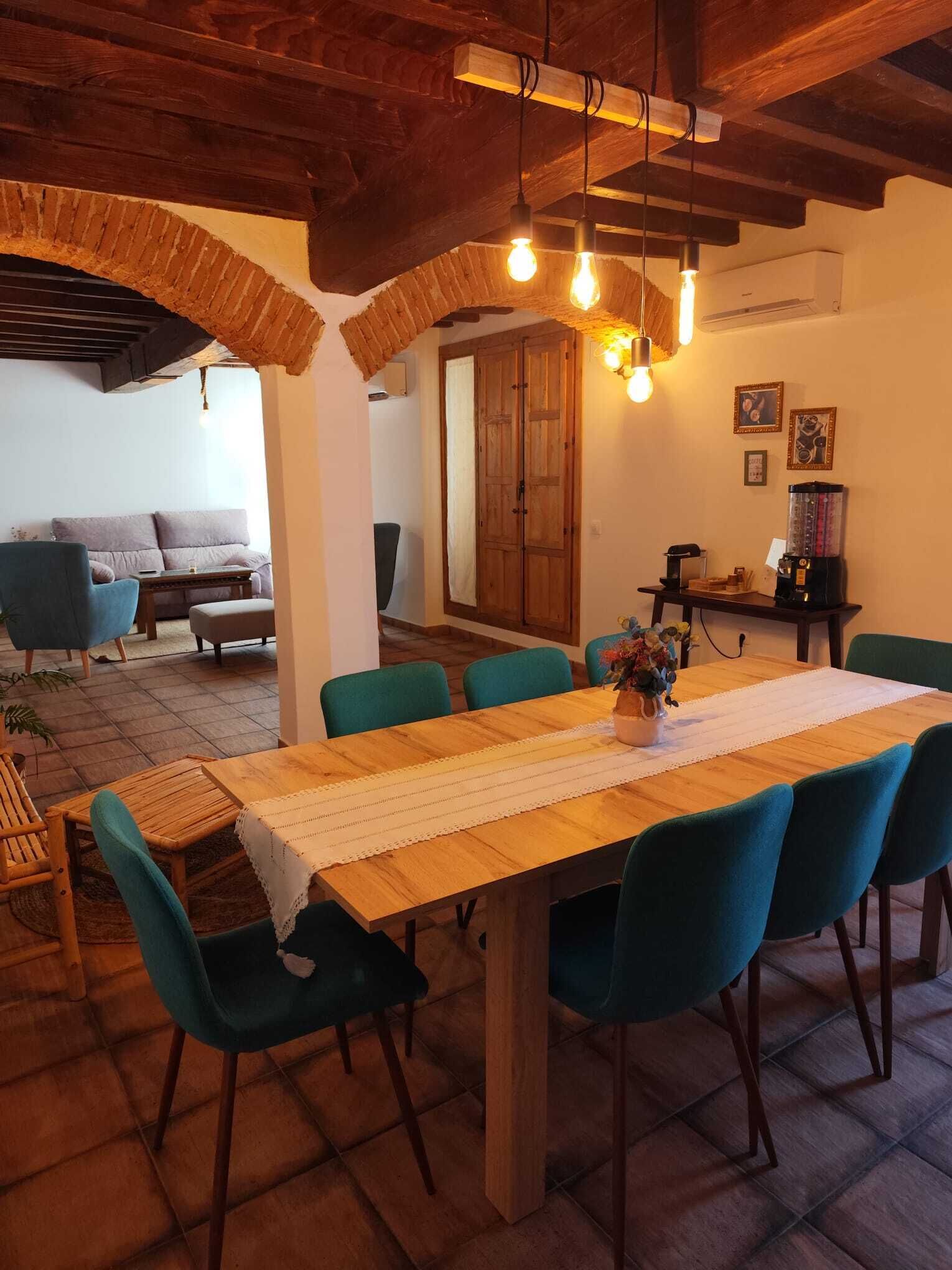 Een eethoek met een houten tafel, teal stoelen en hangende lampen.