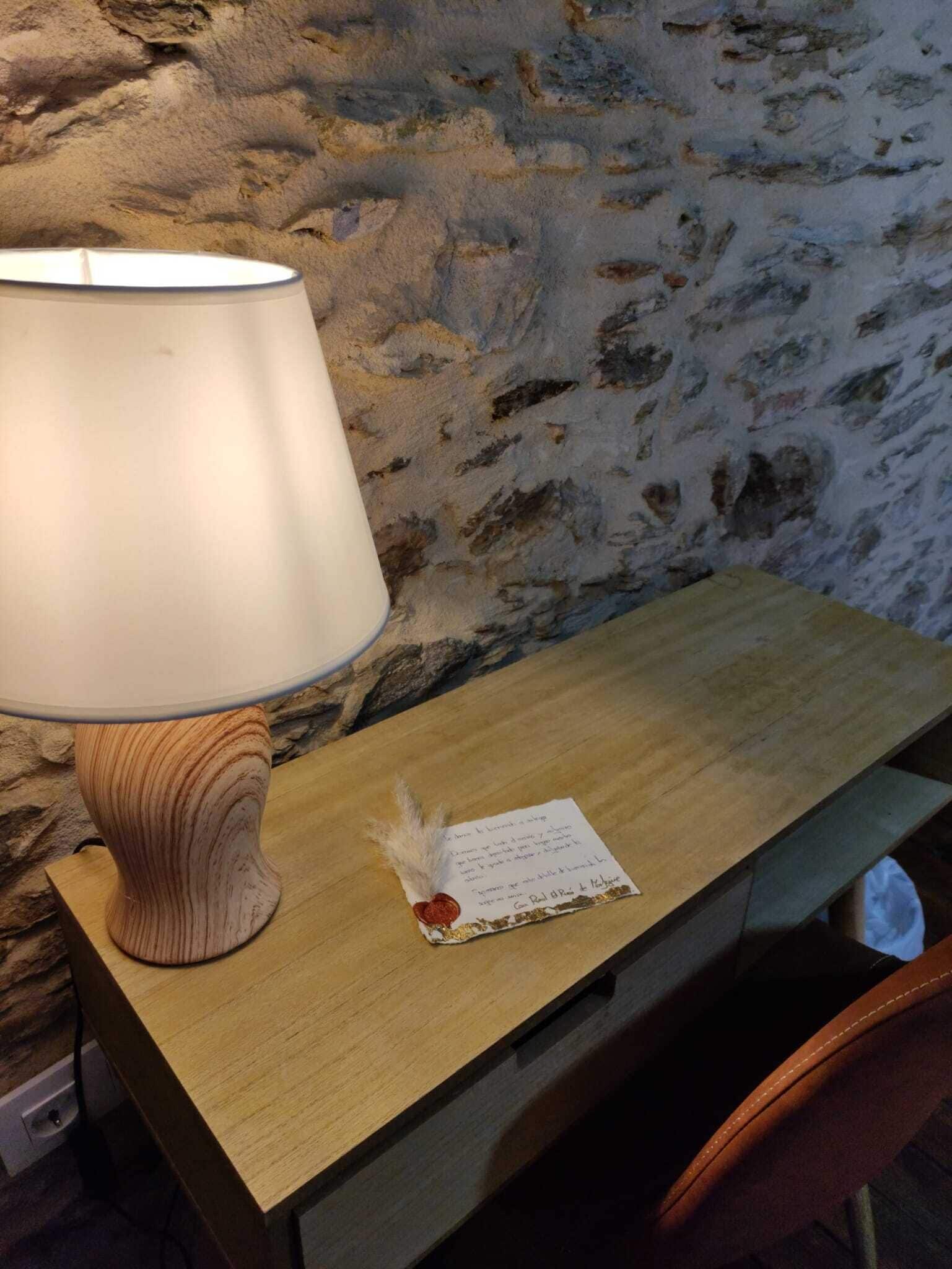 Un escritorio de madera con una lámpara, un adorno pequeño y un papel con texto.