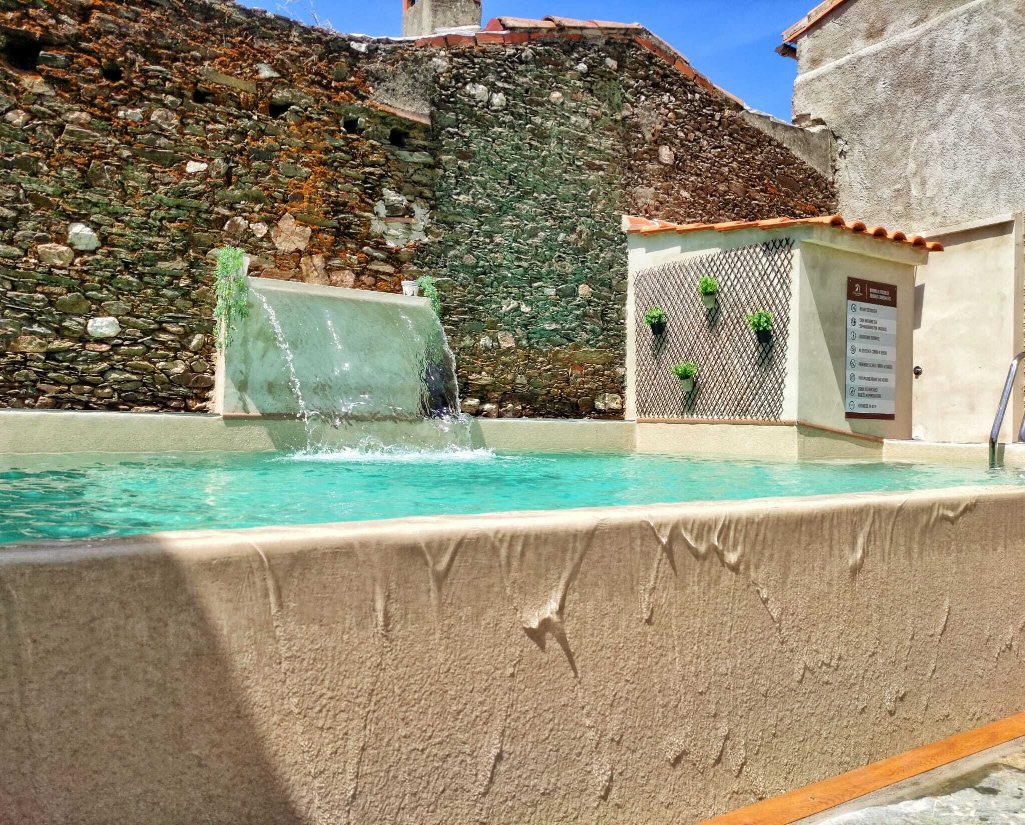 Una piscina con una cascada, rodeada de muros de piedra y un techo de tejas.