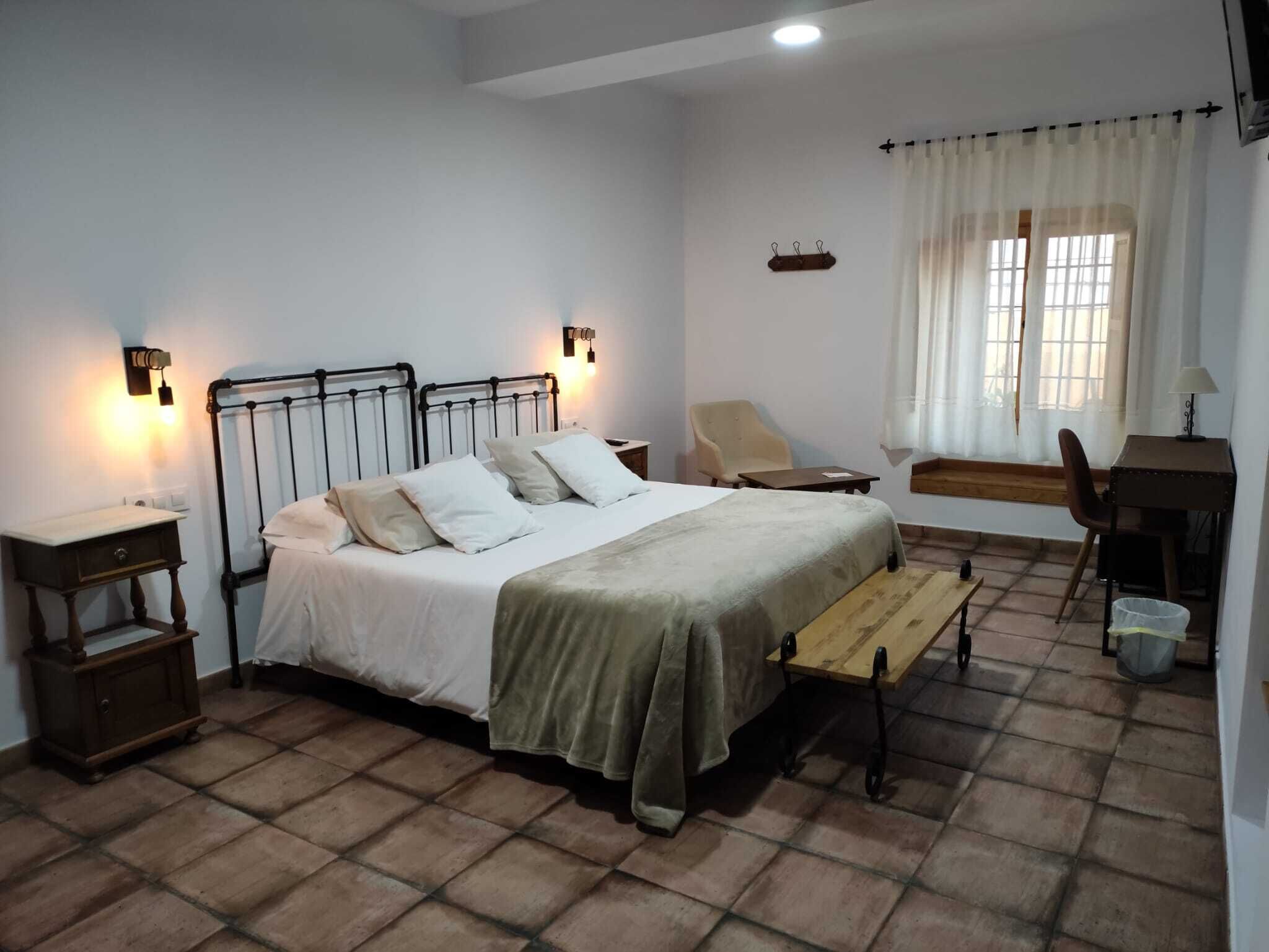 A bedroom with a bed, bedside tables, a chair, a desk, and a window with curtains.