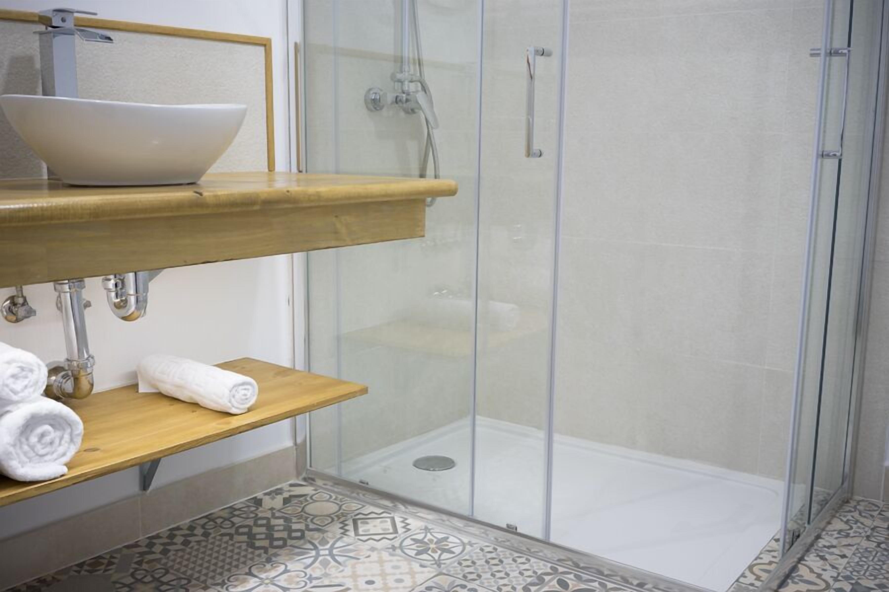A bathroom with a glass shower enclosure, a wooden vanity with a white basin, and patterned floor tiles.