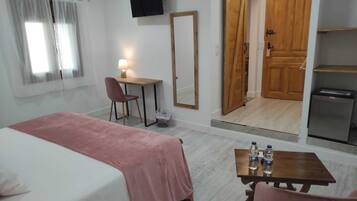 A bedroom with a bed, a desk, a chair, a table with water bottles, a TV, and a wardrobe.