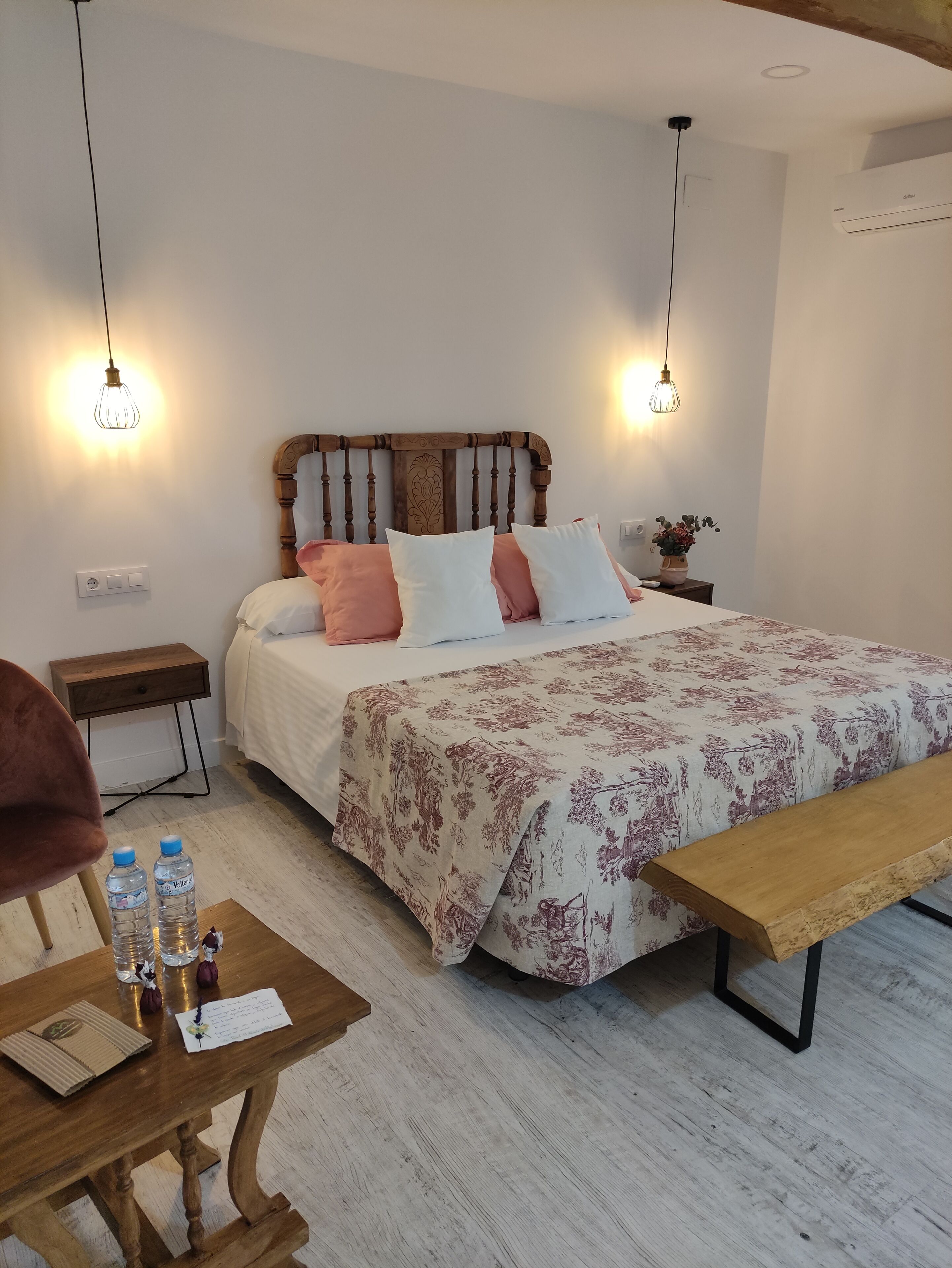 A neatly arranged bedroom with a wooden bed, bedside tables, a bench, and a bedside lamp.