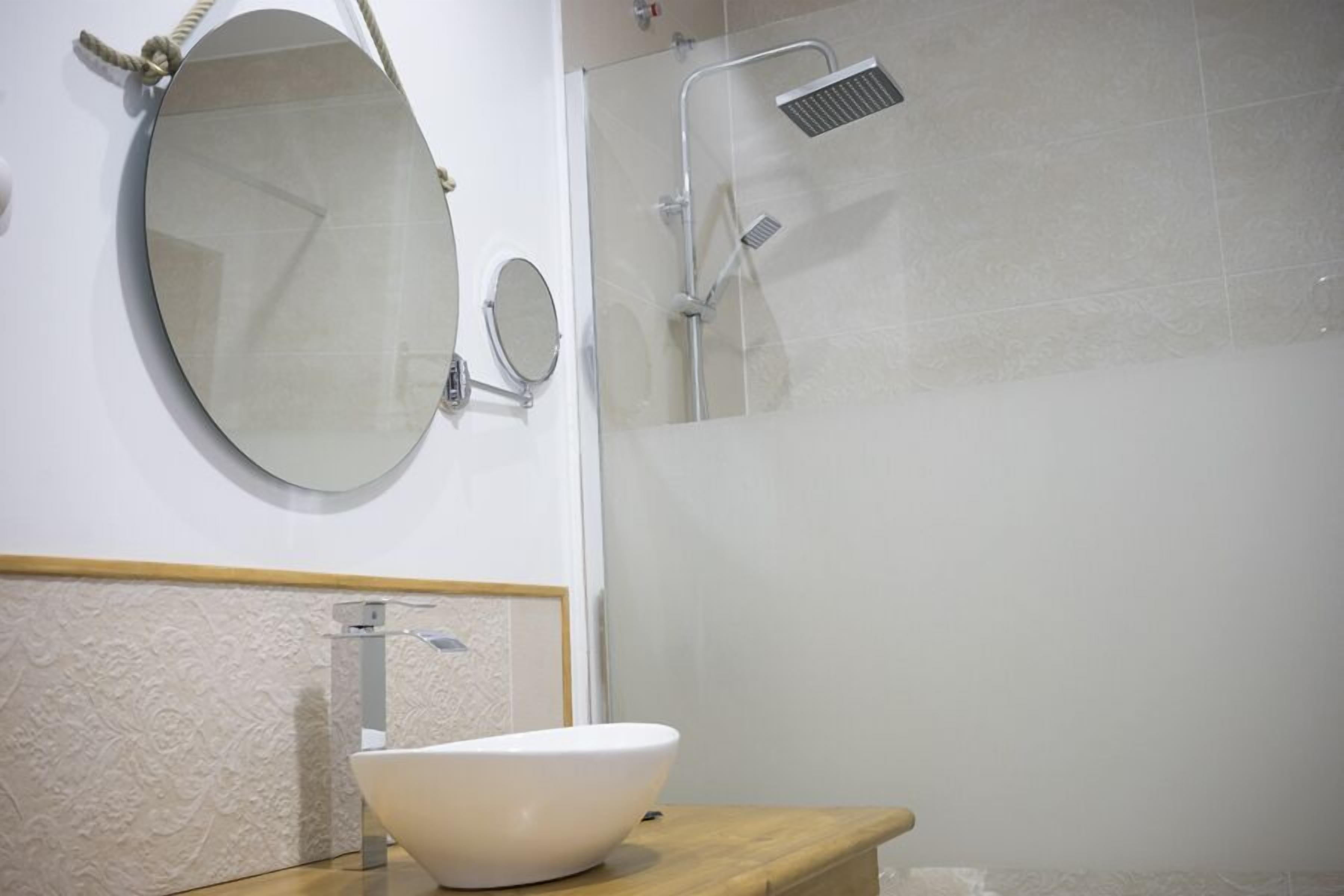 Ein Badezimmer mit einem runden Spiegel, einem kleinen runden Spiegel, einem weißen Waschbecken und einer Dusche mit Glasabtrennung.