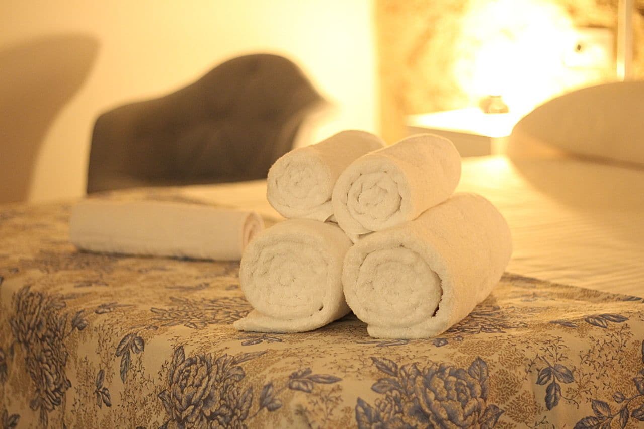 Ein ordentlich bezogenes Bett mit einer floralen Tagesdecke und einem Stapel weißer, aufgerollter Handtücher.