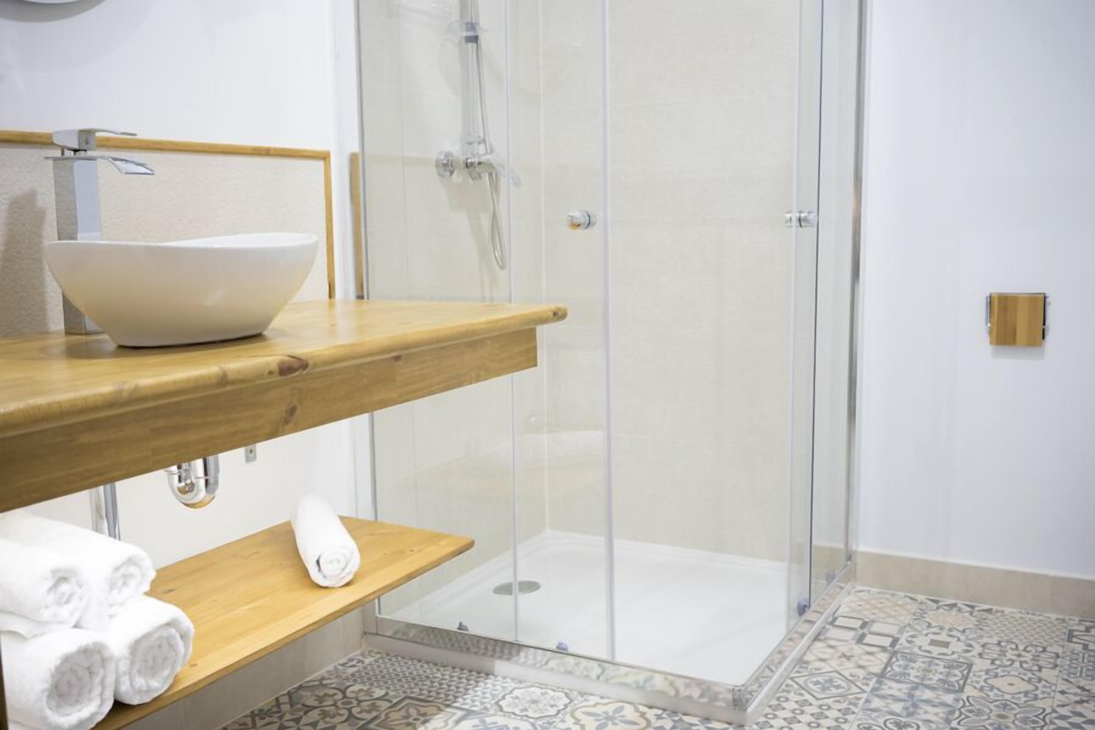 Un baño con tocador de madera, un lavabo blanco y mampara de ducha de vidrio.