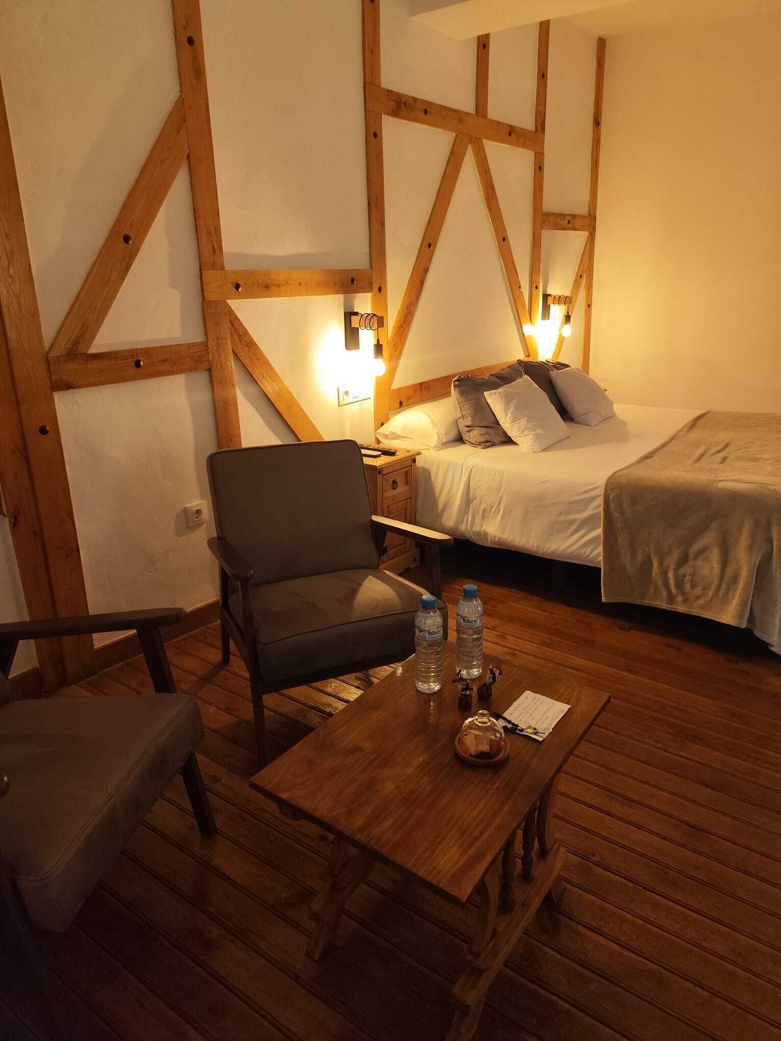 Quarto aconchegante com cama, uma cadeira e uma mesa com garrafas de água.