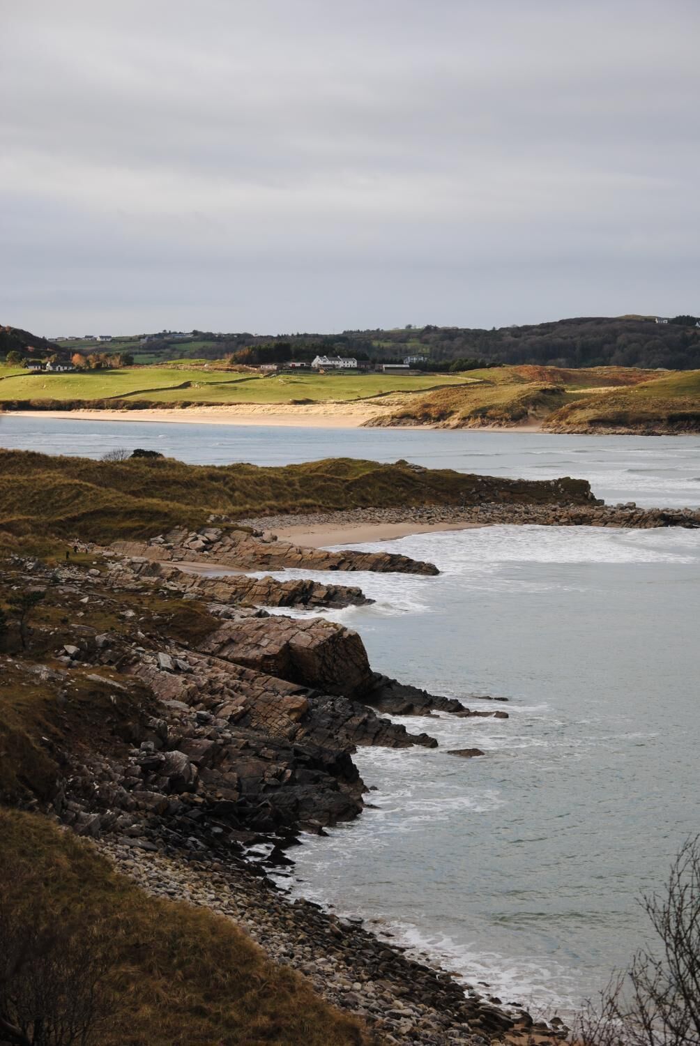 Un paisaje costero con costas rocosas, una playa de arena y casas a lo lejos.