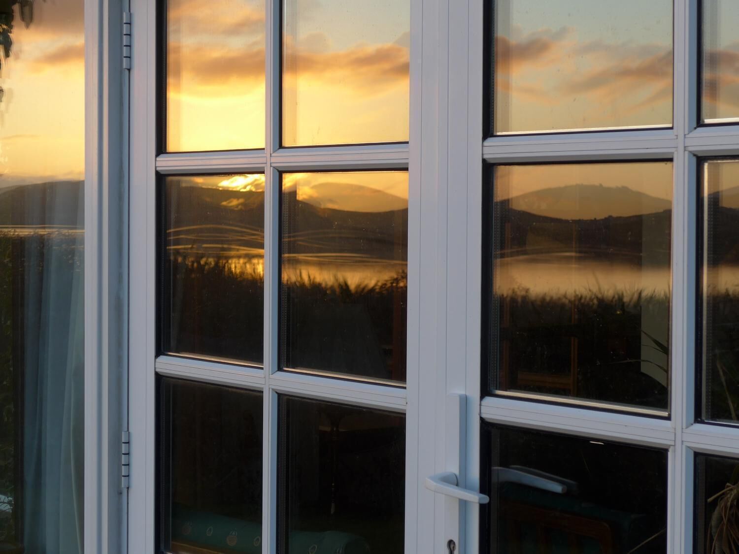 A window with a view of a sunset over a lake and mountains.
