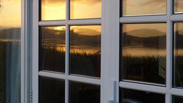 A window with a view of a sunset over a lake and mountains.
