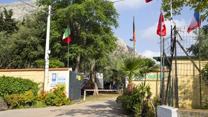 A gated entrance with a sign indicating a camping area, surrounded by lush greenery and a mountain backdrop.