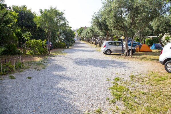 Un camino de grava que conduce a un campamento con tiendas y coches aparcados a un lado de la carretera.