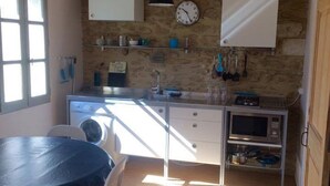 A compact kitchen with a dining area, featuring a stone wall, wooden beams, a clock, and basic appliances. - Duplex character cottage  (Grillon)