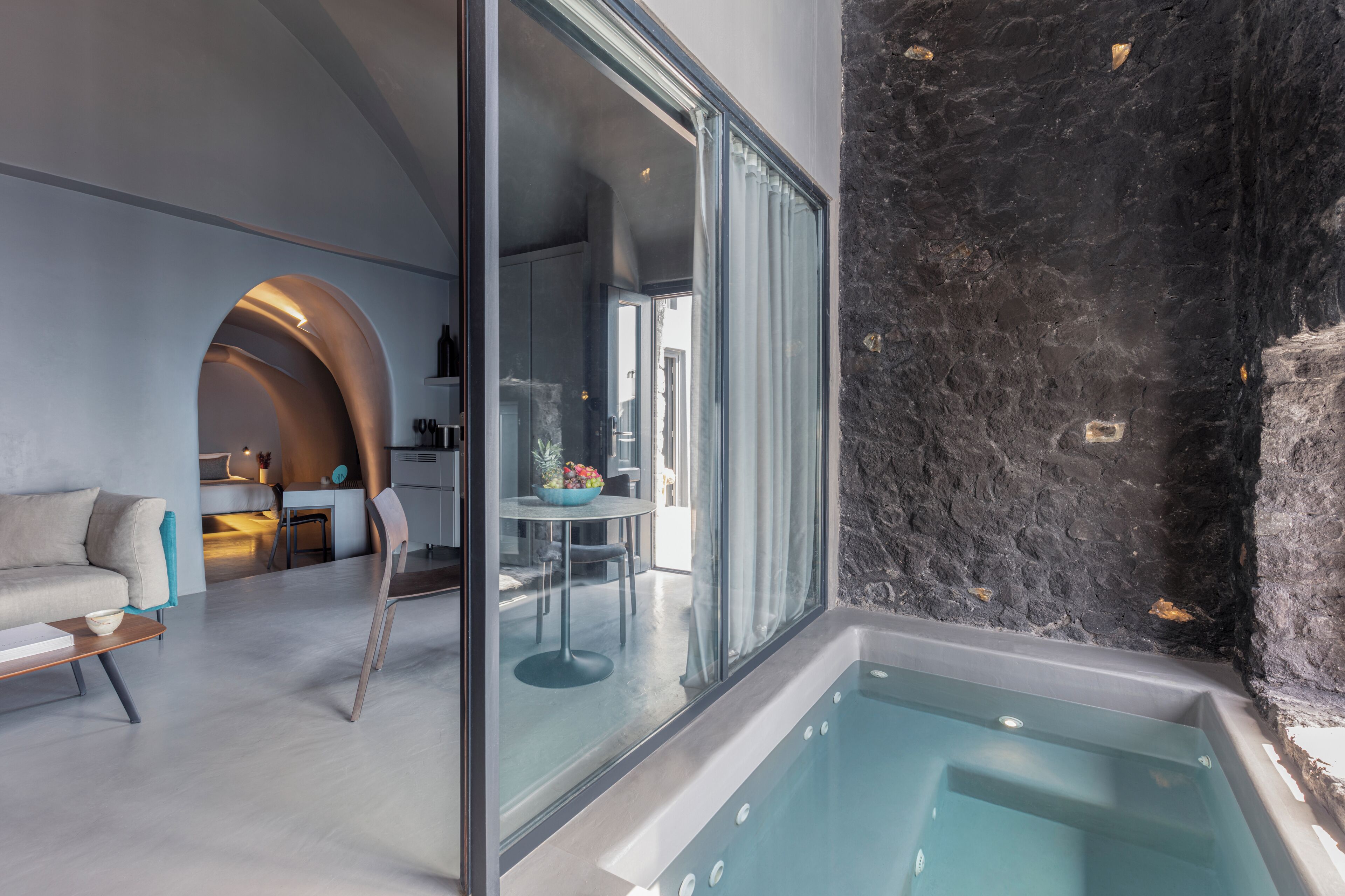 A modern interior with a glass-enclosed jacuzzi, a dining area, and a kitchen visible through the glass.