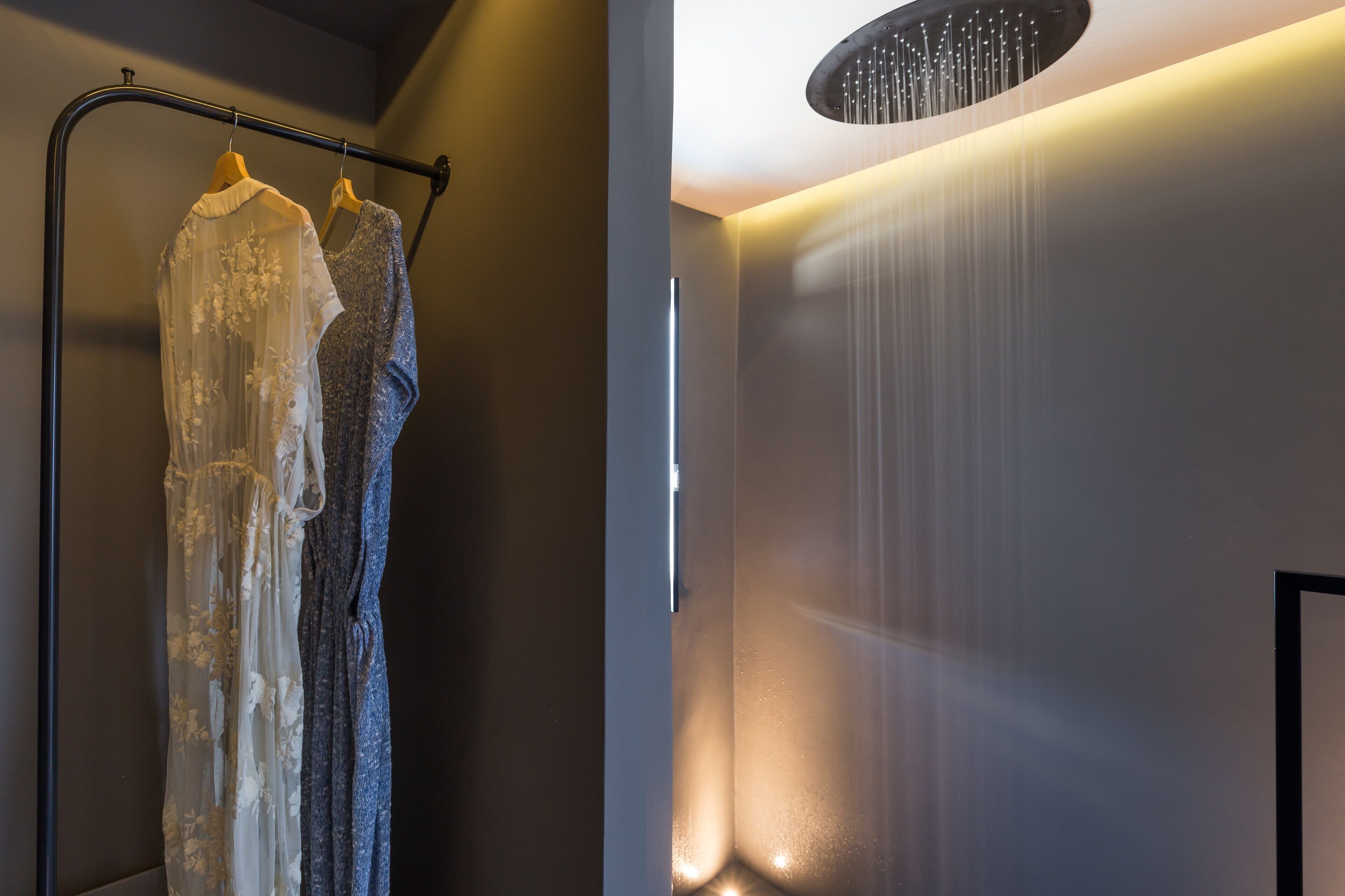 A modern interior with a clothing rack holding dresses, a wall-mounted light fixture, and a door with a frosted glass panel.