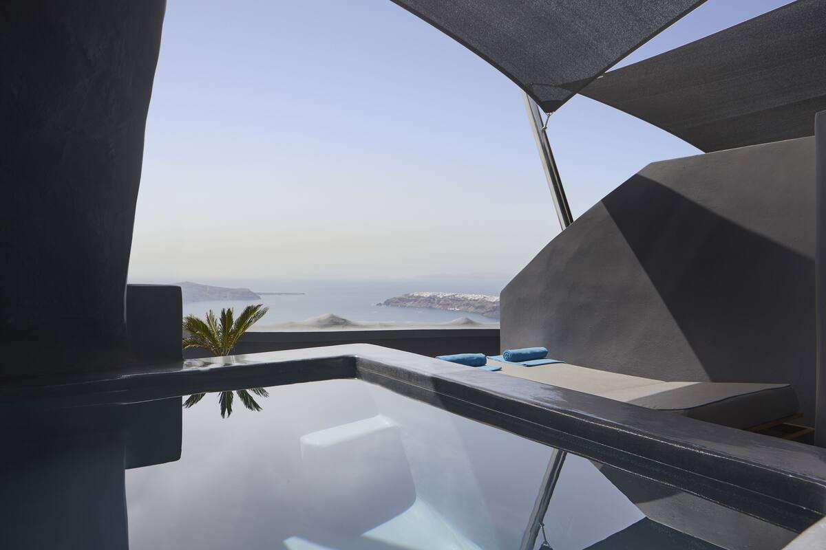 A modern, minimalist room with a glass bathtub and a view of the sea.