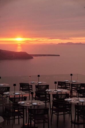 Un restaurant doté de tables et de chaises disposées pour accueillir les clients, offrant une vue sur une étendue d’eau et sur la terre ferme au loin.
