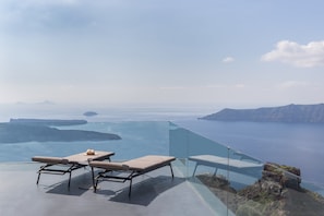 Une piscine à débordement en verre, dotée de chaises longues et d’une table, offrant une vue panoramique sur l’océan.