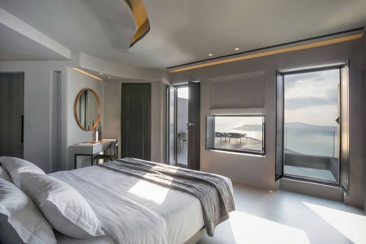 A modern bedroom with a large bed, a desk, and a view of the sea.