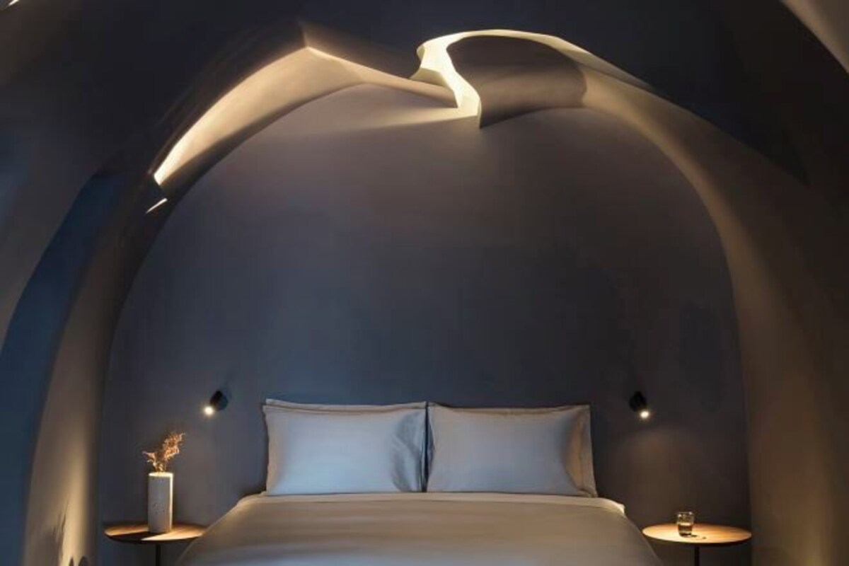 Une chambre moderne avec un plafond incurvé, un lit, des tables de chevet et des lampes fixées au mur.