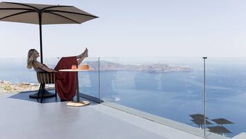 Eine Person entspannt sich auf einem Balkon mit Tisch und Sonnenschirm, mit Blick auf eine malerische Seelandschaft und das entfernte Land.