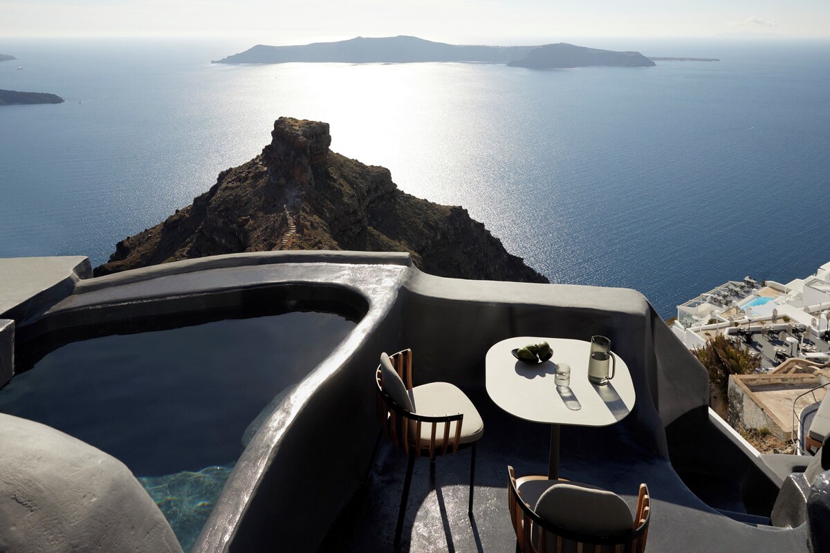 Une terrasse avec une table et des chaises, offrant une vue panoramique sur la mer et une île lointaine.