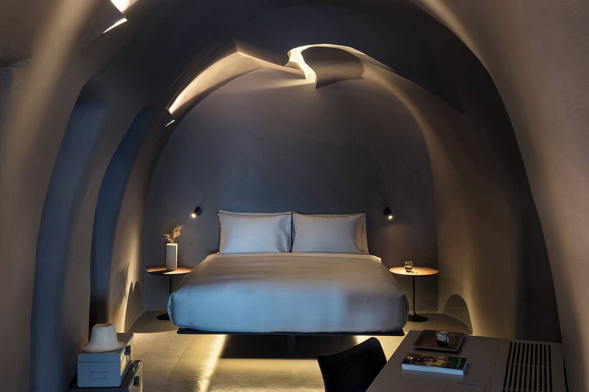 A modern bedroom with a curved ceiling, a large bed, bedside tables, and a small table with a lamp.
