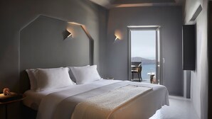 Un dormitorio moderno con una cama grande, una mesita de noche, una silla y vistas al mar.