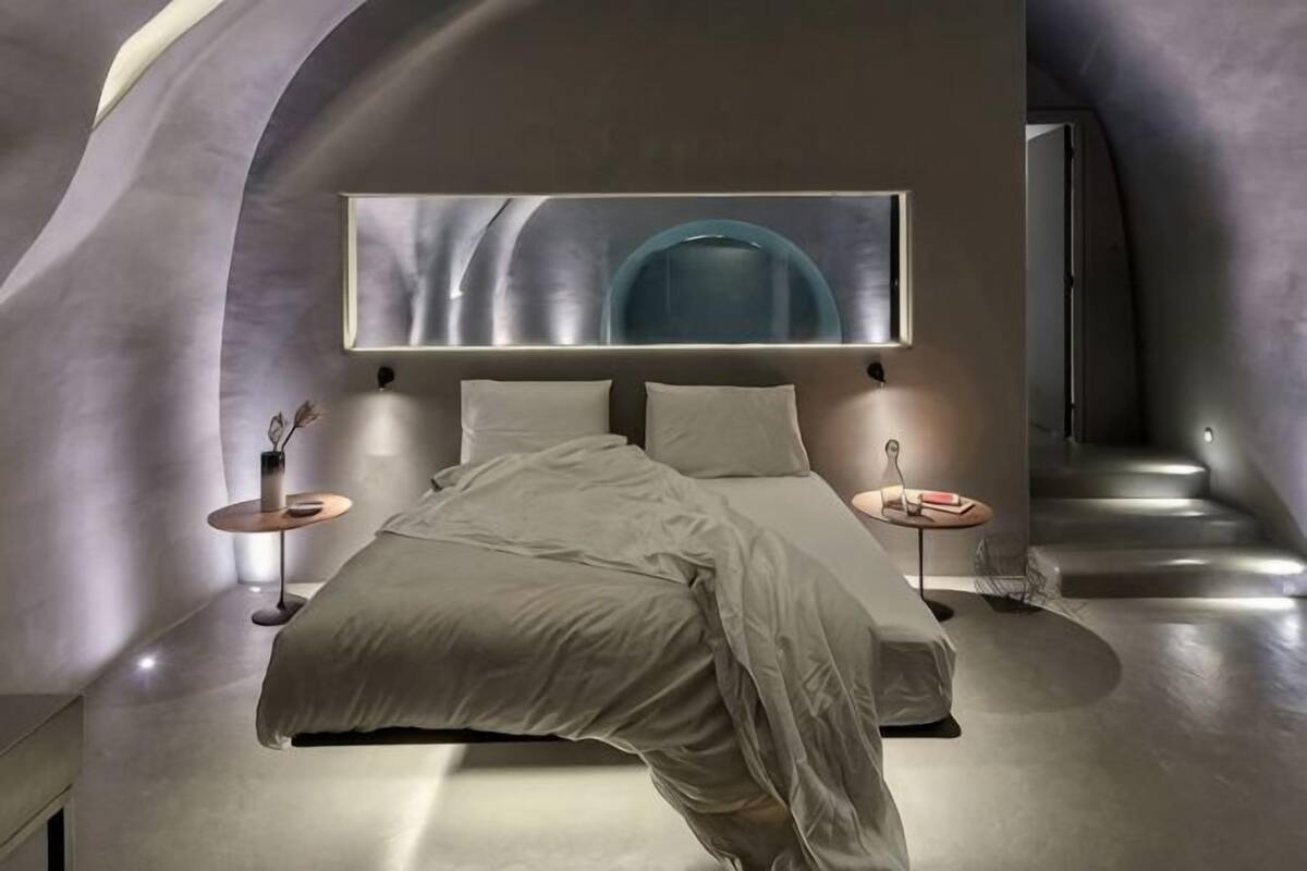 A modern bedroom with a curved ceiling, a large bed, bedside tables, and a wall-mounted TV.