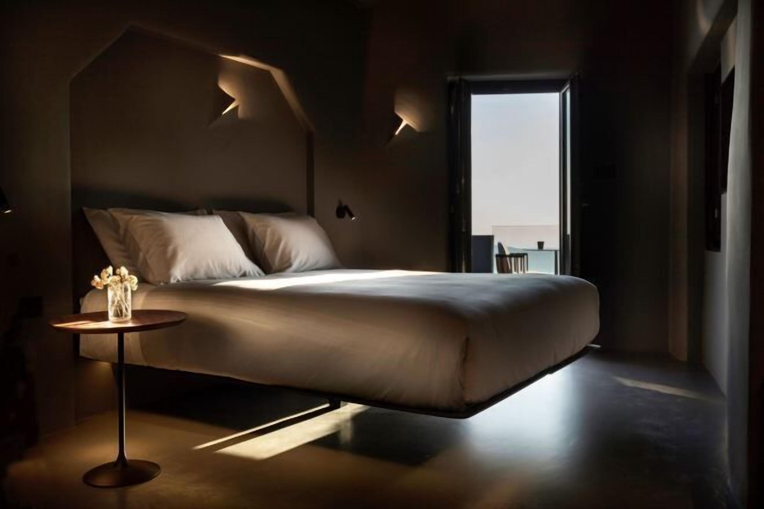 A modern bedroom with a bed, bedside table, and a view of the outdoors.