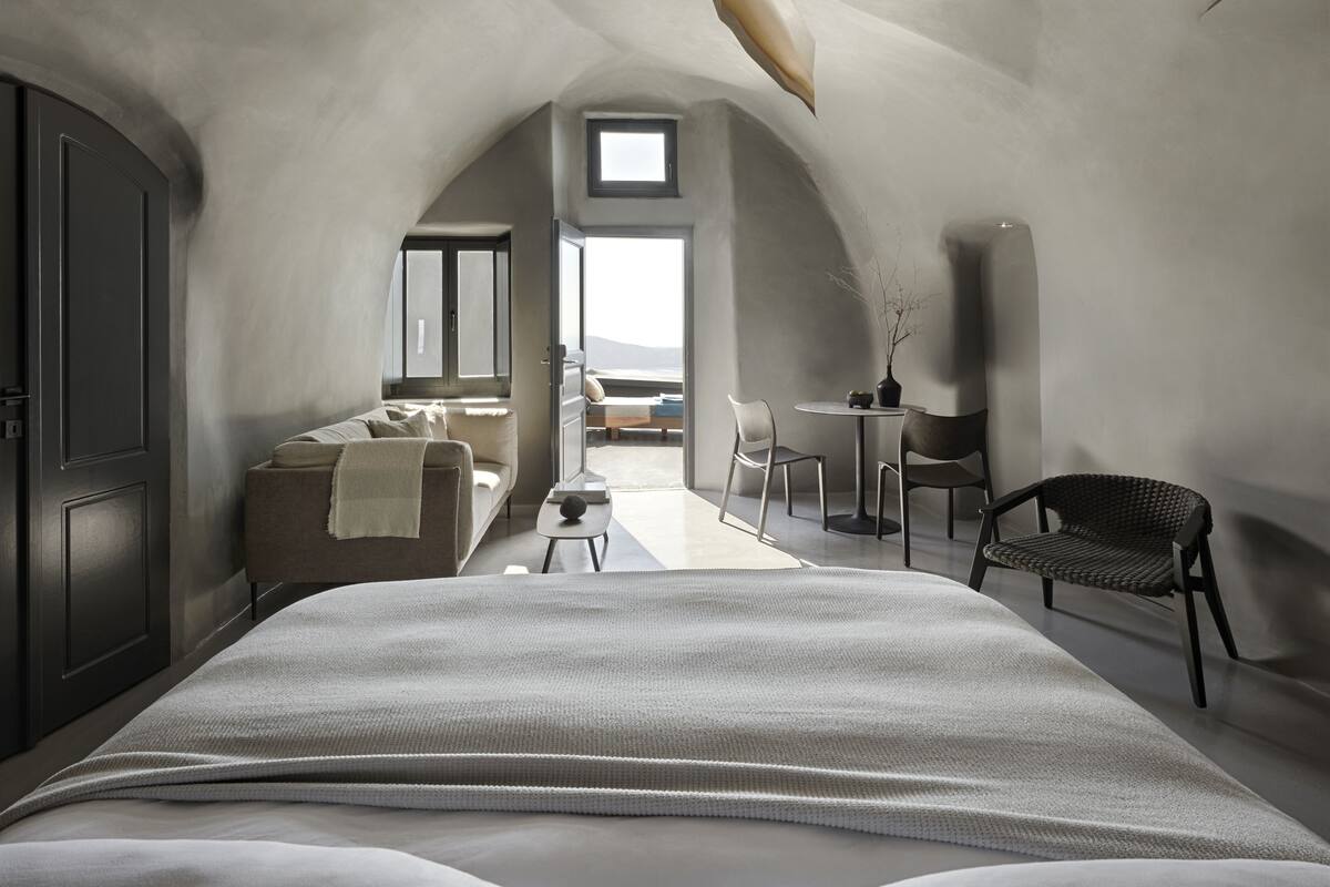 A modern bedroom with a large bed, a desk, and a chair. There is a view of the outdoors through a window.