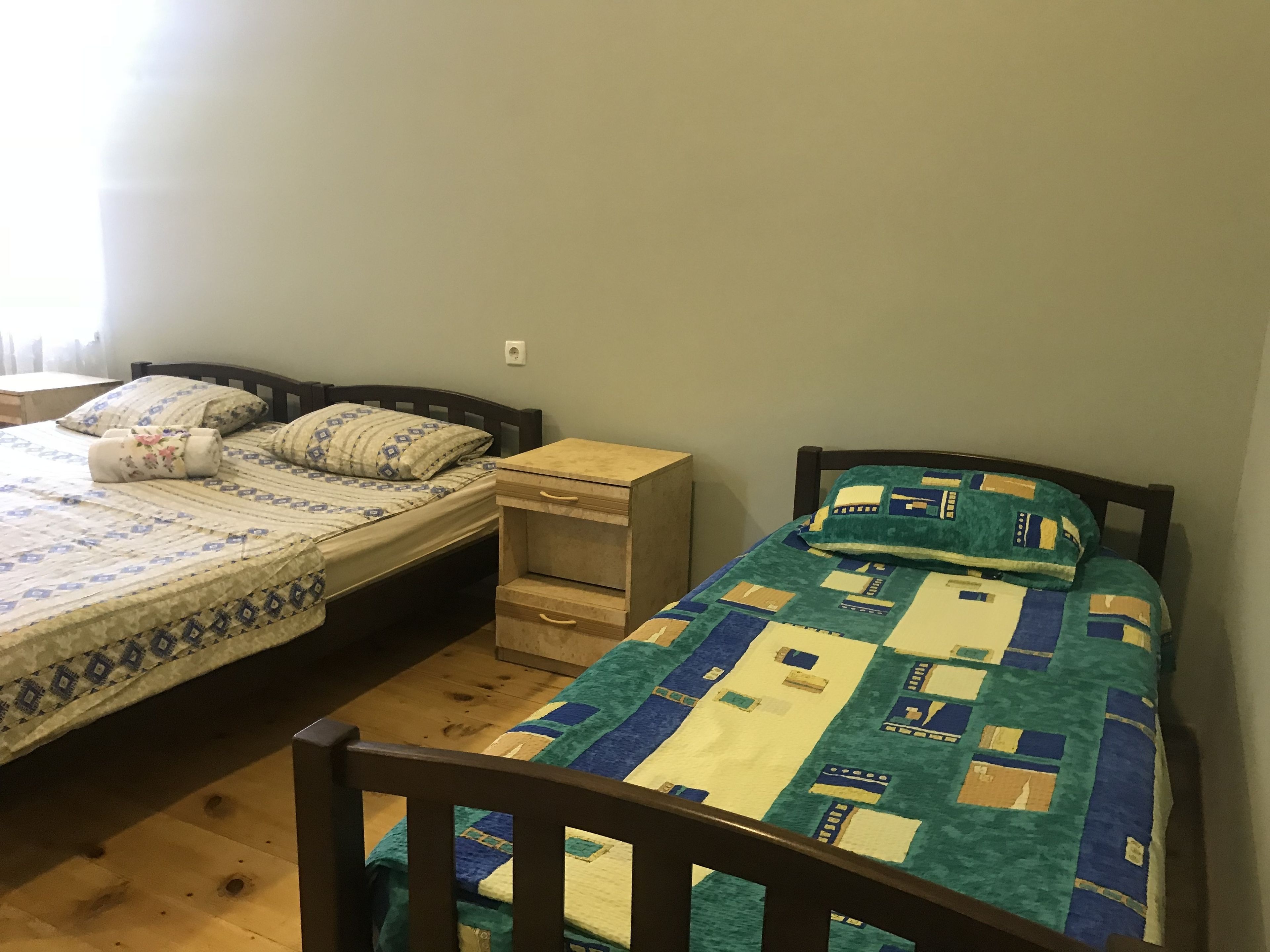 A bedroom with two single beds, each with a wooden headboard, a small bedside table, and a drawer.