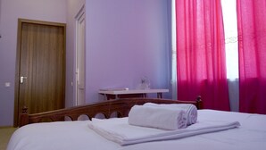A neatly made bed with white linens and a rolled towel, a wooden headboard, a small white table with a glass object, and a wooden door. - Mimino (Kutaisi)